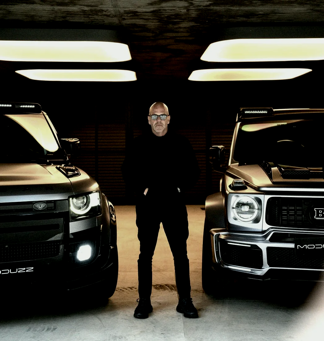 Fundador da MODUZZ entre um Land Rover Defender e um GWM Tank 300 transformados